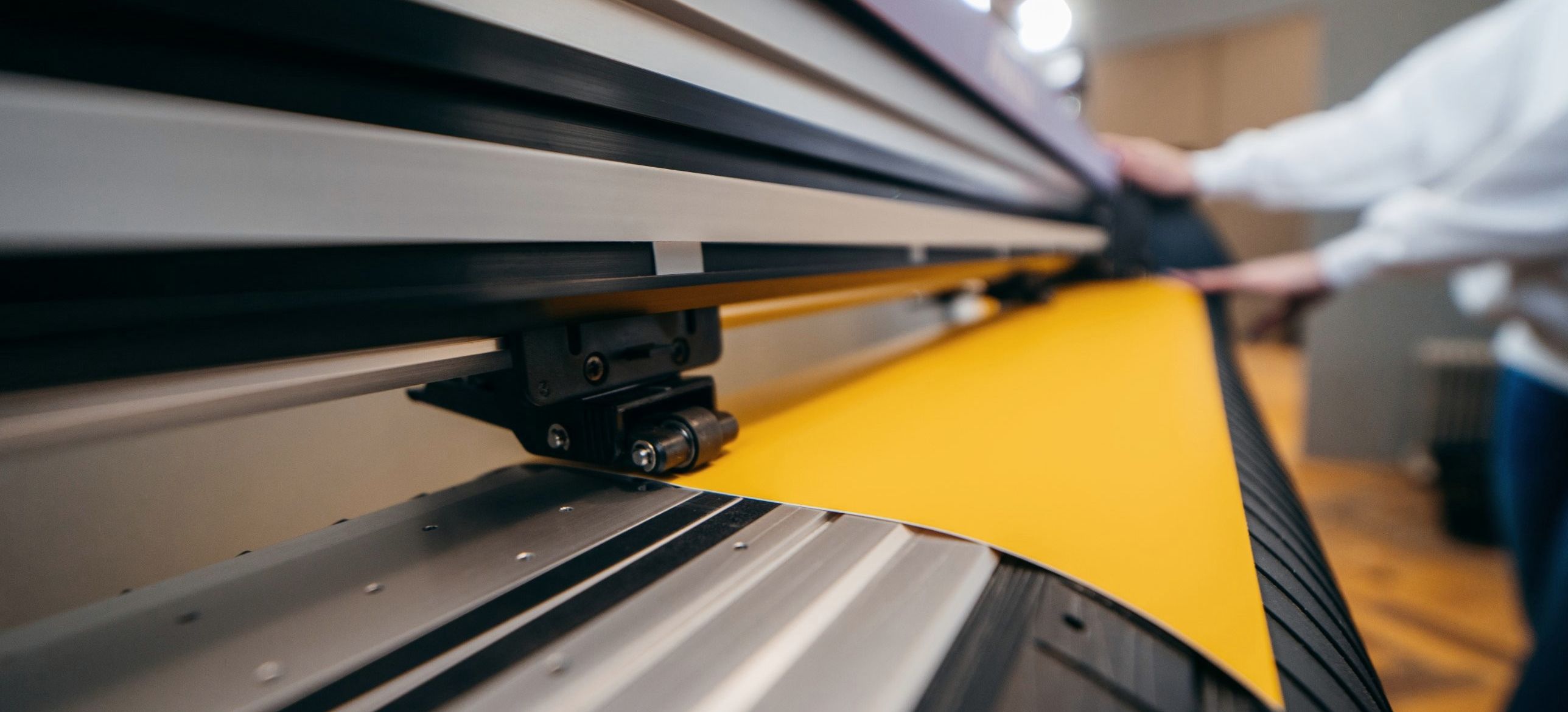 Ochre vinyl feeding through a wide-format printer as an operator guides the roll