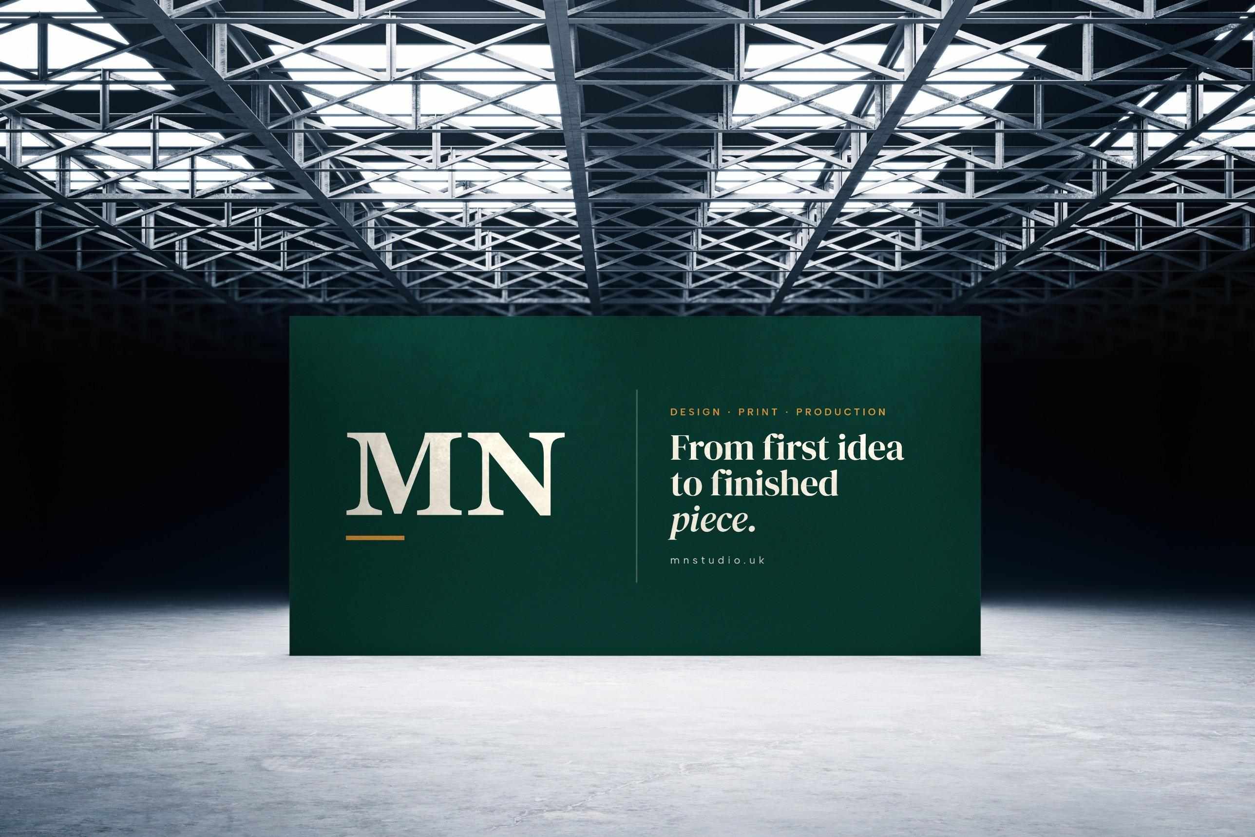 A large green MN Studio backdrop reading “From first idea to finished piece” beneath a steel-truss ceiling