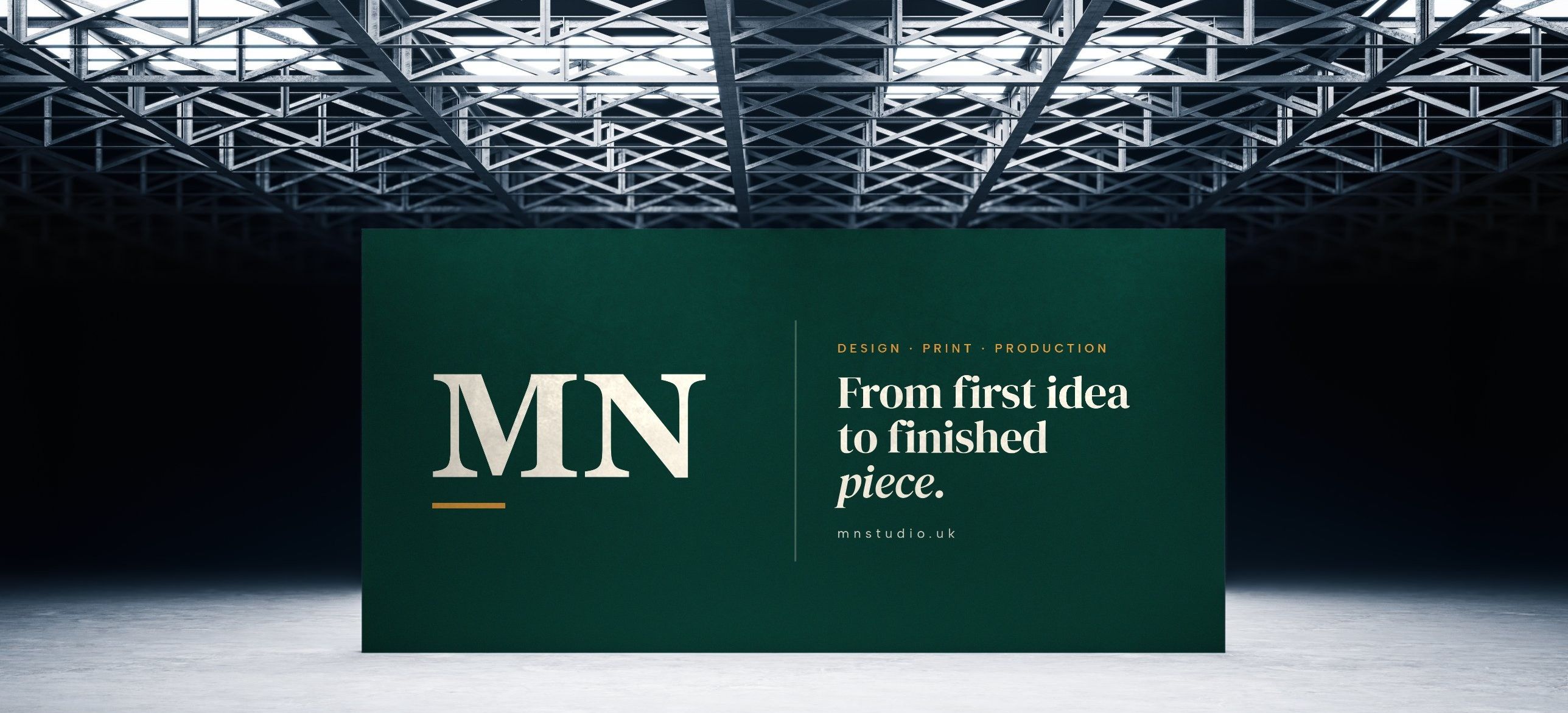A large green MN Studio backdrop reading “From first idea to finished piece” beneath a steel-truss ceiling