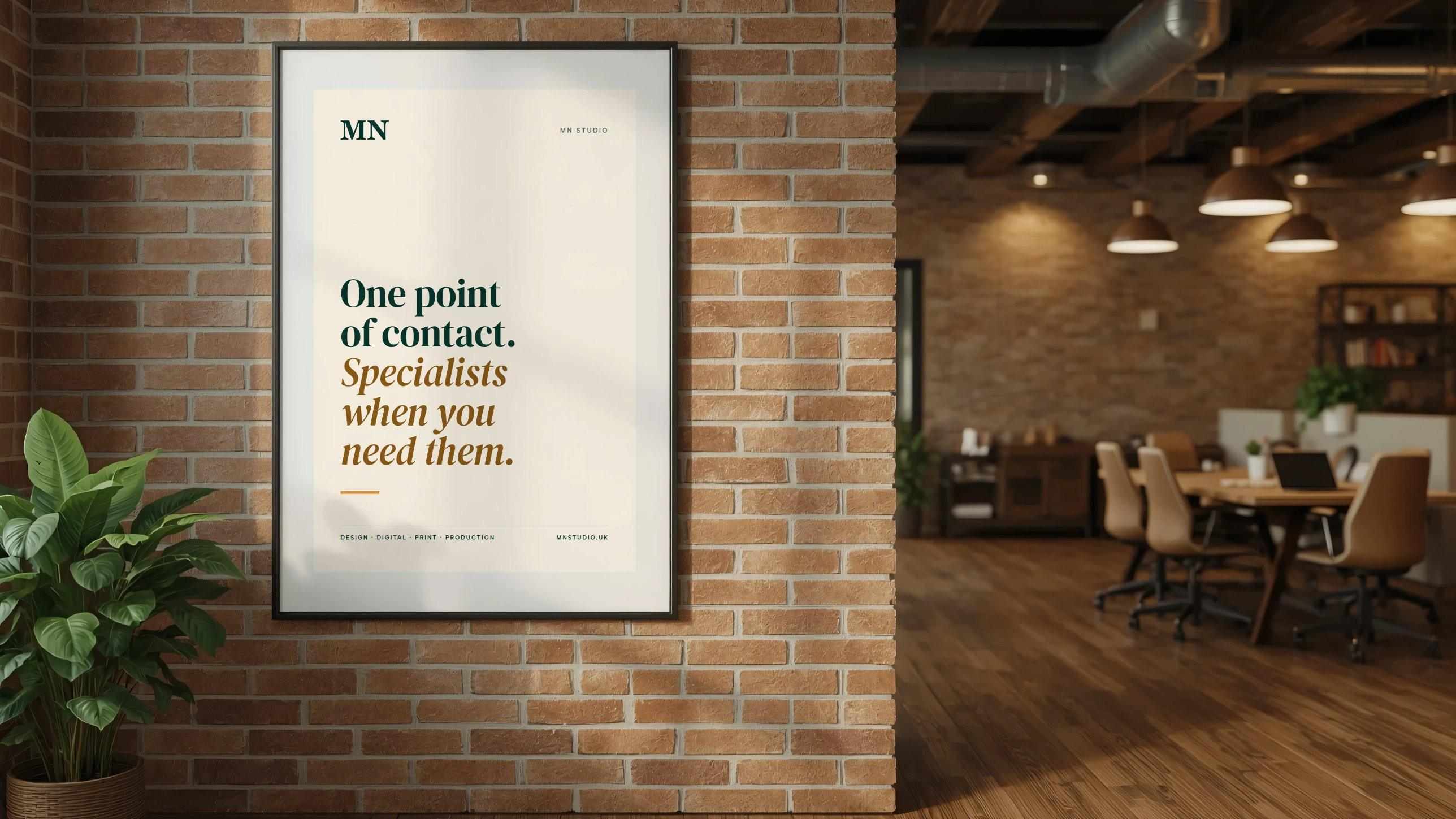 A framed cream MN Studio poster on a brick studio wall: “One point of contact. Specialists when you need them.”