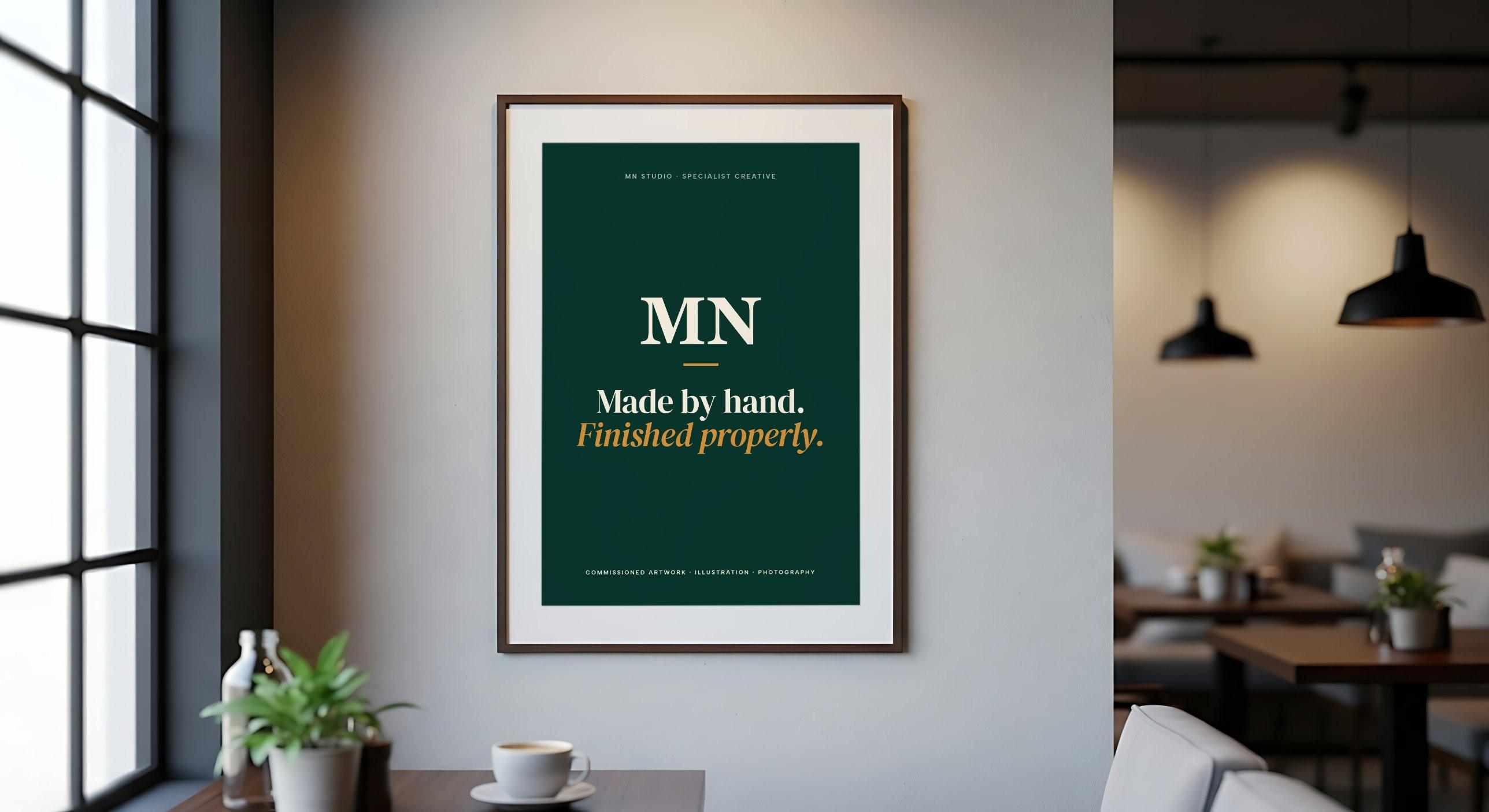 A framed green MN Studio poster in a café: the MN monogram above “Made by hand. Finished properly.”