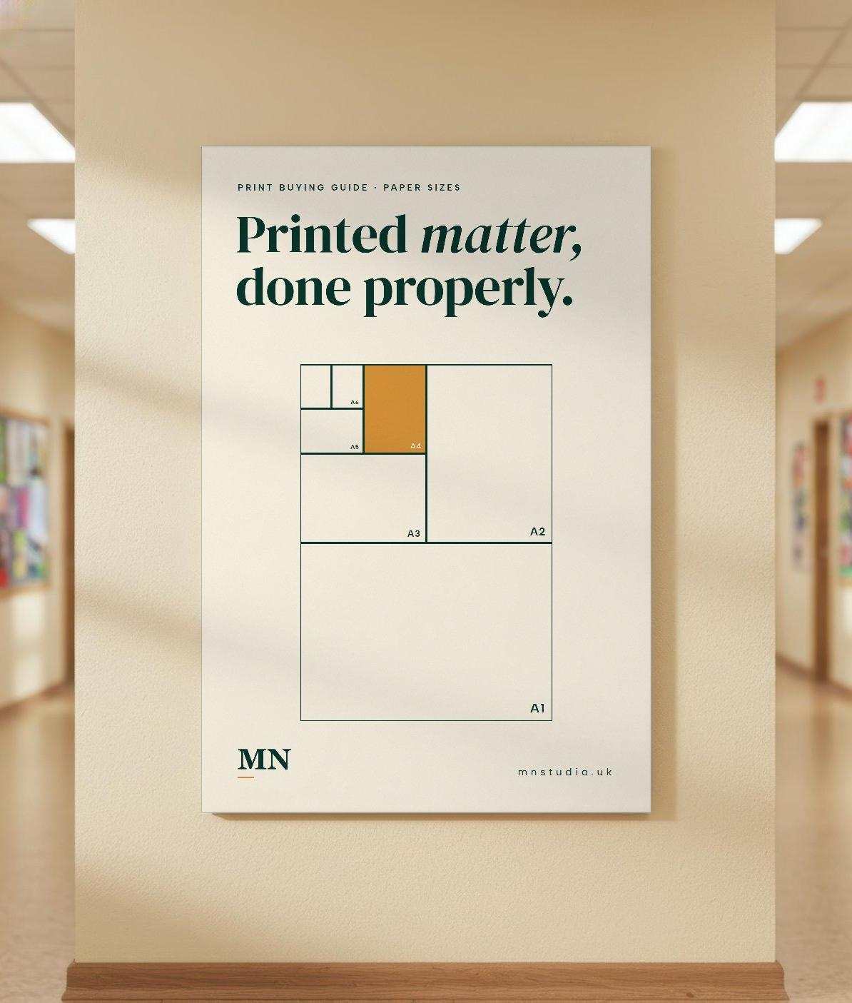 A cream MN Studio poster showing A-series paper sizes, hung on a corridor wall